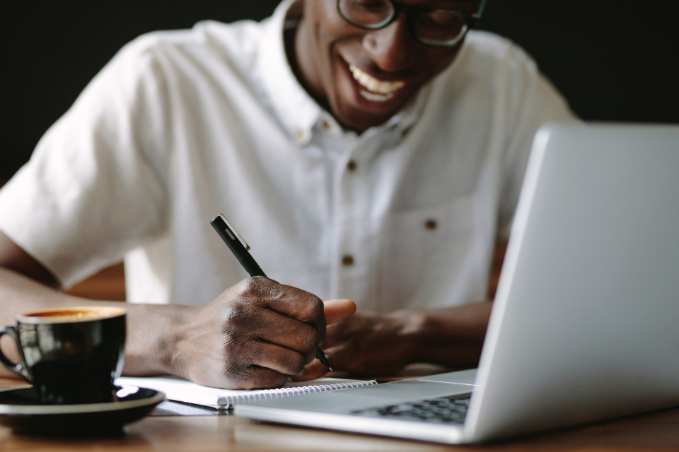 black man smiling and writing in notebook